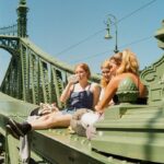 three women sitting on a bridge looking at something