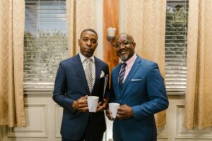 Two businessmen in formal attire stand indoors holding mugs, symbolizing professionalism and camaraderie.