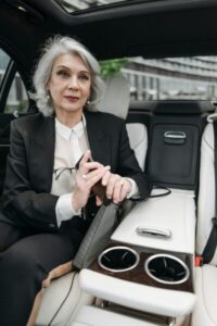 Senior woman in a business suit inside a luxury car holding eyeglasses, creating an executive ambiance.