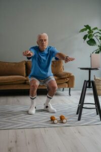 A senior man performing squats with dumbbells on a mat indoors for a healthy lifestyle.